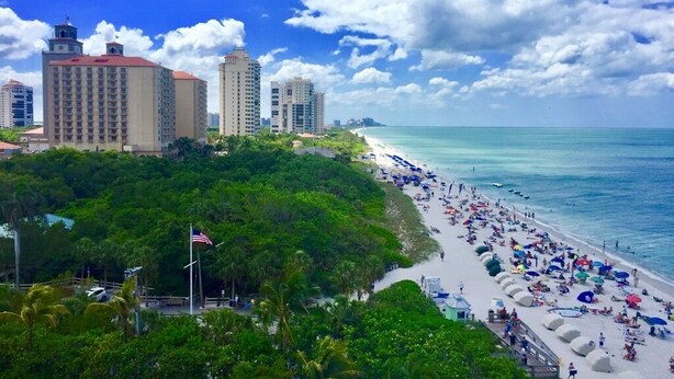 Ein Strand mit einer Reihe hoher Gebäude im Hintergrund, einem klaren Himmel und einer Flagge auf einem Fahnenmast.