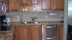 A kitchen with wooden cabinets, a stainless steel refrigerator, and a tiled backsplash. - Crystal Sands Tower Unit 104 - Beachfront (Sarasota)