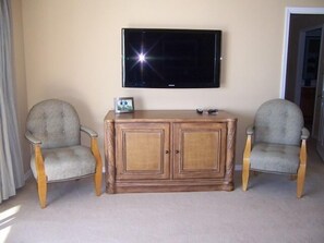 A living room with two armchairs, a wooden cabinet, and a flat-screen TV mounted on the wall.