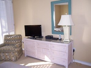 A bedroom with a television, a lamp, a dresser, and a chair.