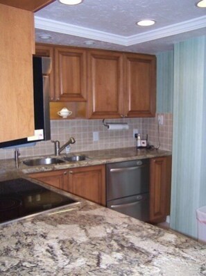 A kitchen with wooden cabinets, a granite countertop, stainless steel appliances, and a tiled backsplash.