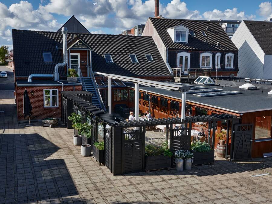 A rooftop terrace with outdoor seating, a brick building, and a white building with a sloped roof.