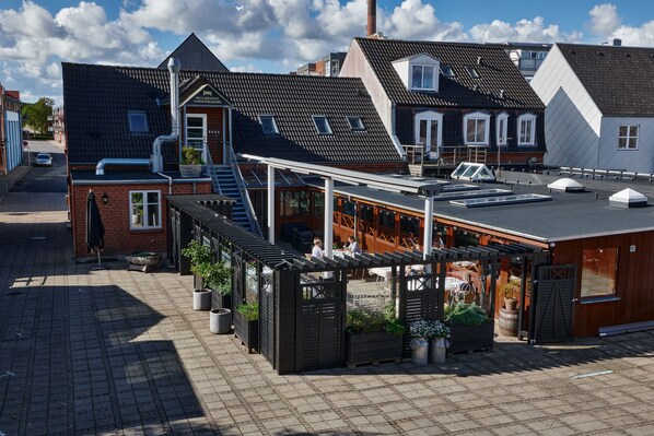 A rooftop terrace with outdoor seating, a brick building, and a white building with a sloped roof.