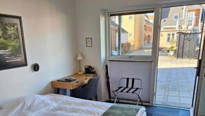 A hotel room with a bed, a desk, a chair, and a view of the street through a glass door. - Hotel Phønix (Holstebro)