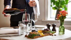 A person pouring wine into a glass, a table with various food items, and a vase with flowers. - Hotel Phønix (Holstebro)