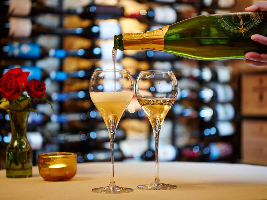 A hand pouring champagne into two glasses on a table.