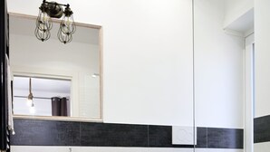 Un baño moderno con un lavamanos blanco, un bidé y un inodoro. Hay un mueble de tocador de madera y un pequeño taburete con texto.