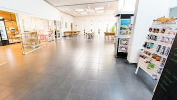 Un espacio interior amplio con suelo de baldosas, una zona de estar con mesas y sillas, y una exhibición de varios productos en estanterías.