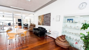 A modern interior with a wooden floor, a black leather sofa, a glass display case, and a dining area with a round table and chairs. - Plexus Hytterne (Holstebro)