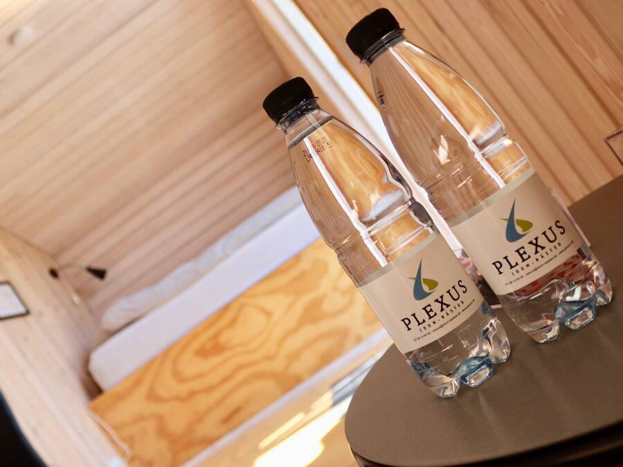 Two bottles of water labeled 'PLEXUS' on a wooden table in a room with wooden walls and a white ceiling.