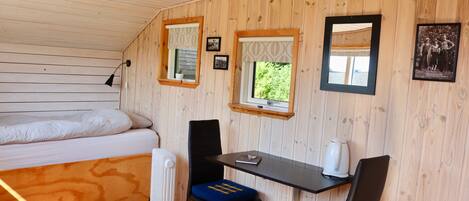 A cozy room with a bed, a table, two chairs, a radiator, and a window with a view.