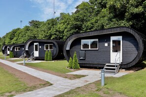 A row of modern, curved cabins with external steps and small trees in front. - Plexus Hytterne (Holstebro)