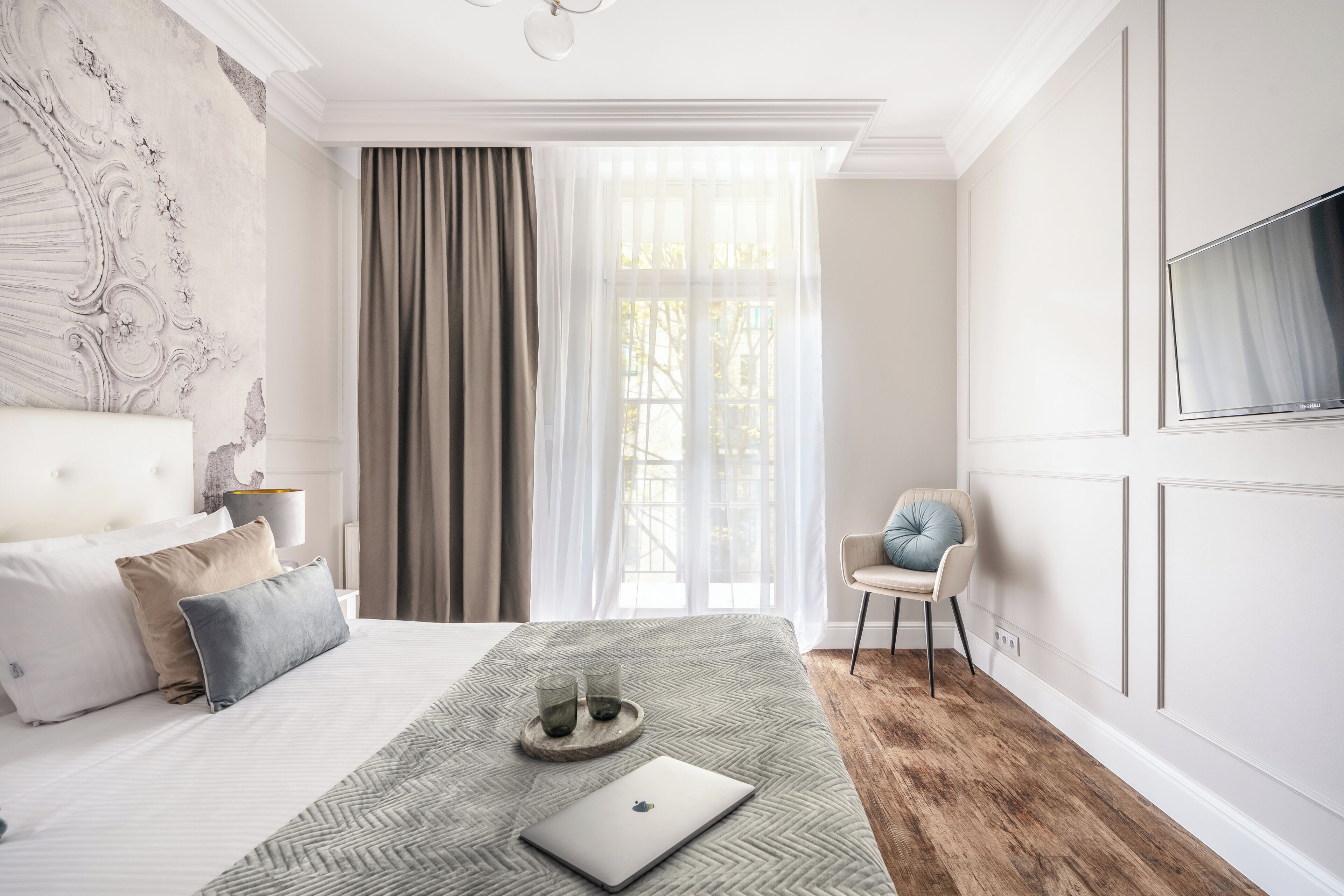 Une chambre moderne avec un grand lit, un ordinateur portable posé sur le lit, une chaise et un téléviseur fixé au mur.