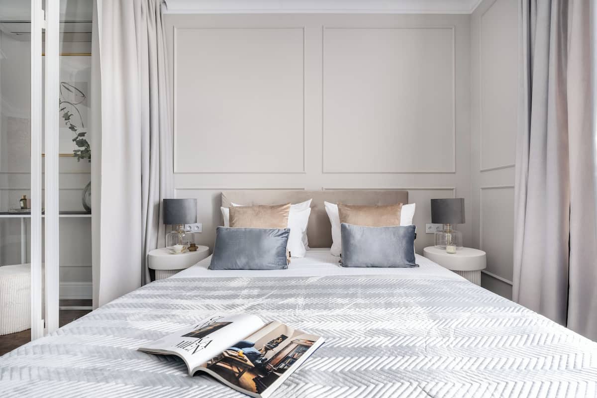 A neatly arranged bedroom with a large bed, two bedside tables with lamps, and a magazine on the bed.