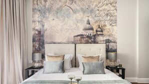 A hotel room with a large bed, two nightstands, a lamp, a tray with two glasses, and a wall mural of a cityscape.