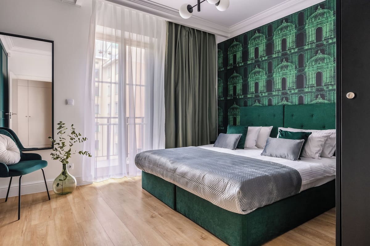 A bedroom with a large bed, a green upholstered headboard, and a green patterned wall.