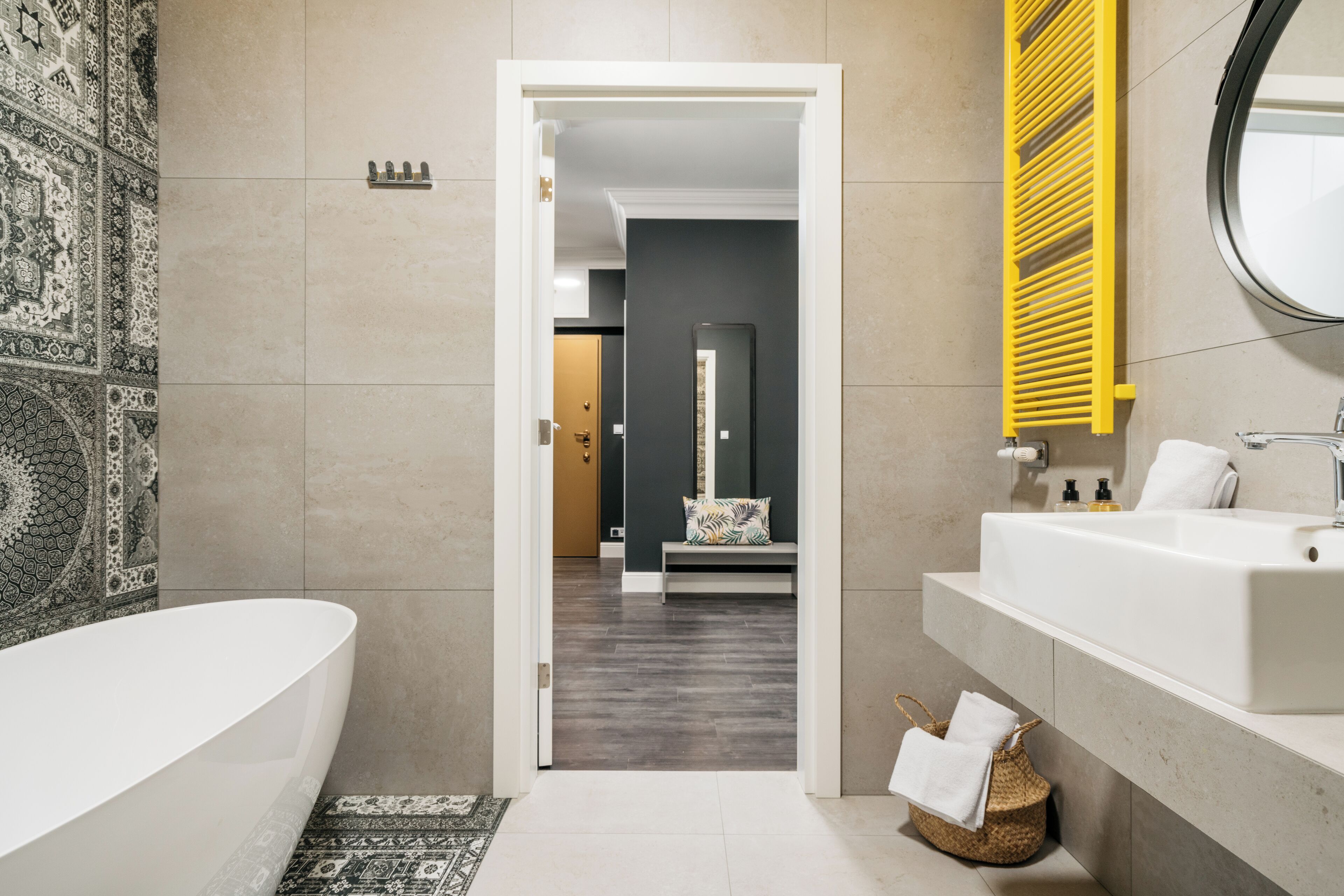 A modern bathroom with a large bathtub, a vanity with a mirror, and a patterned rug on the floor.