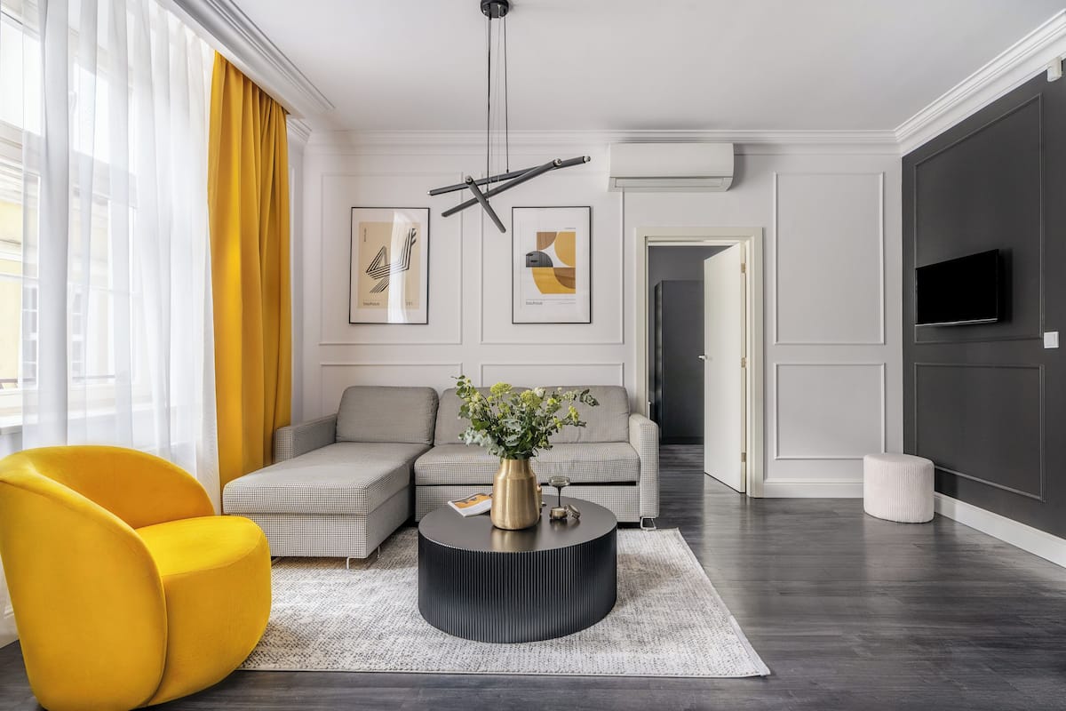 A modern living room with a sofa, a yellow armchair, a round coffee table with a vase, and framed artwork on the wall.