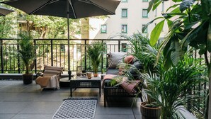 A balcony with outdoor seating, potted plants, and a large umbrella.