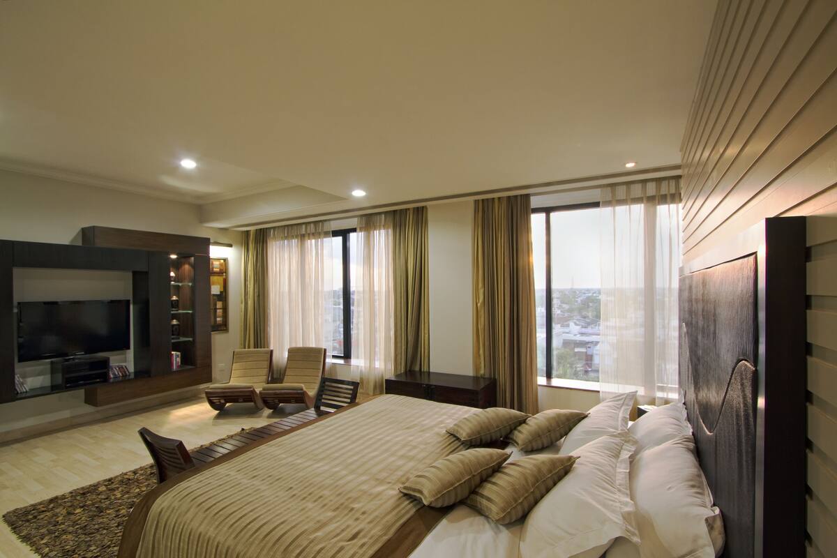 Quarto de hotel moderno com uma cama grande, televisão de tela plana, área de estar e vista para a cidade.
