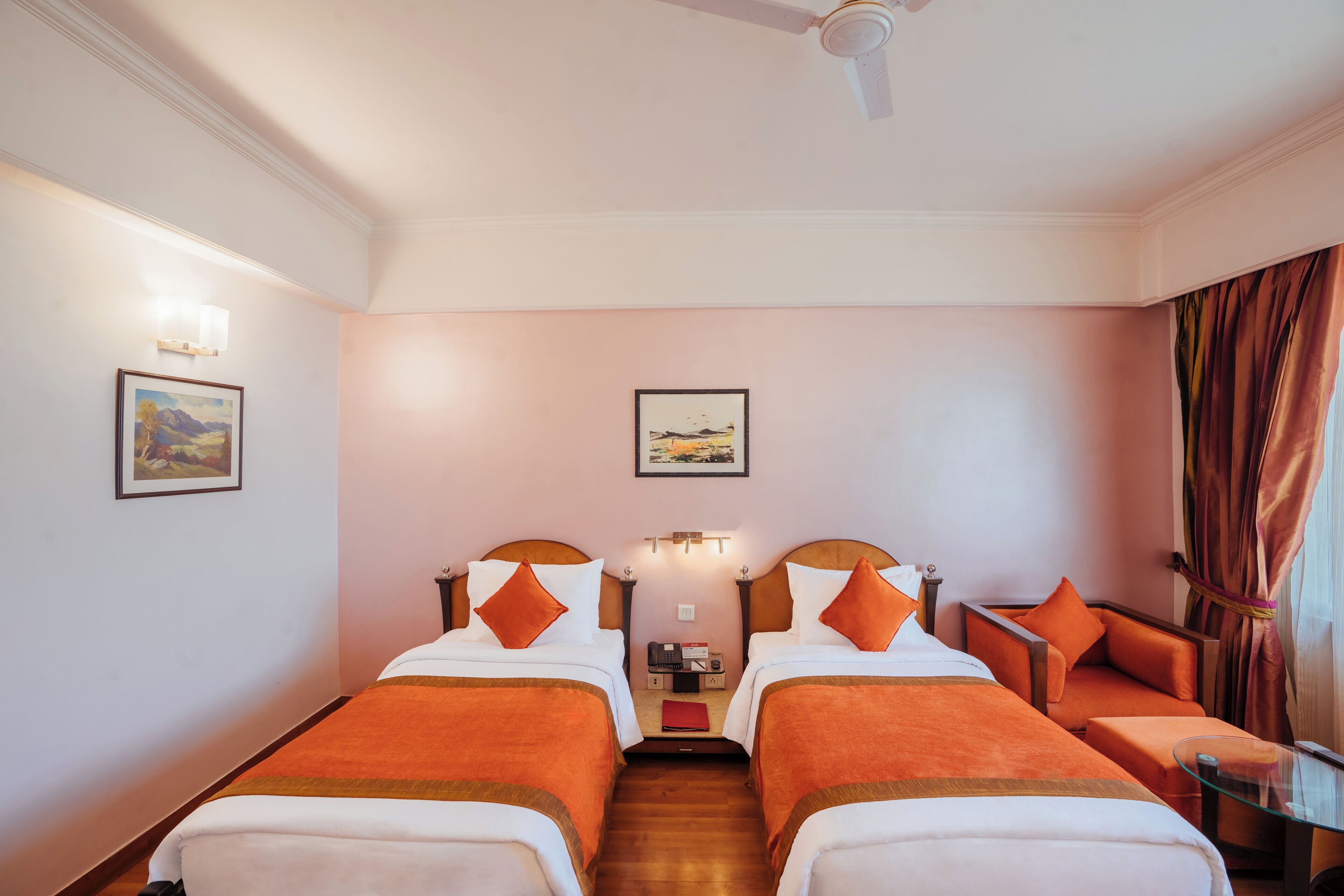 A hotel room with two beds, a sofa, a small table, and a ceiling fan.