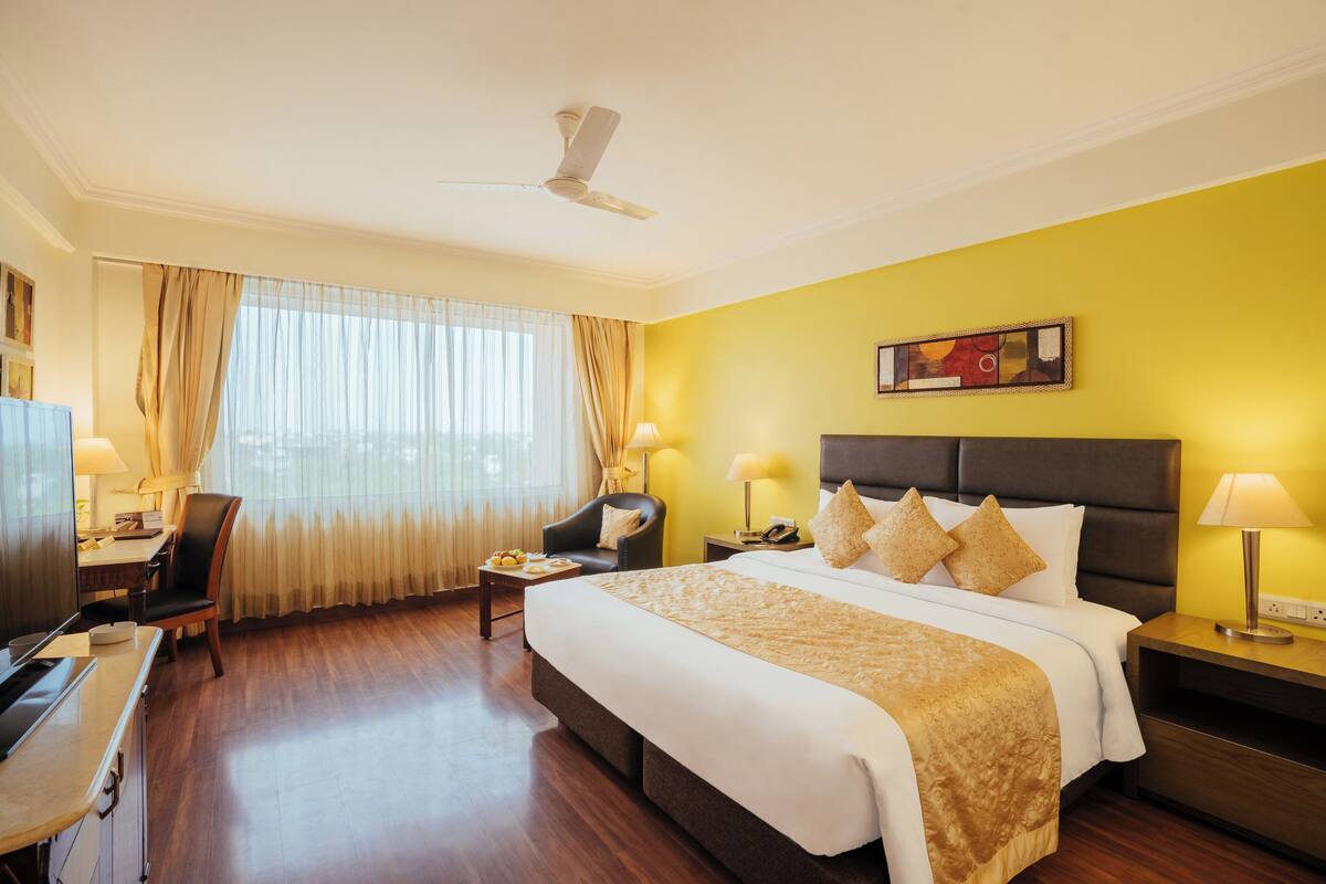 Quarto de hotel com cama, escrivaninha, cadeira, televisão e ventilador de teto.