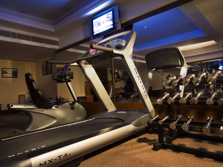Un gimnasio en casa con cinta de correr, pesas y televisor montado en la pared.