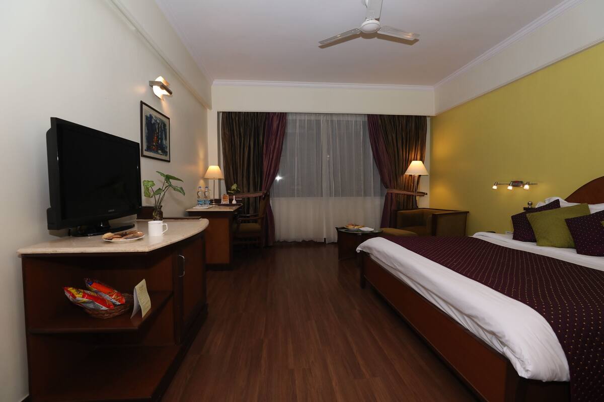 Quarto de hotel com cama, escrivaninha, televisão e ventoinha no teto.