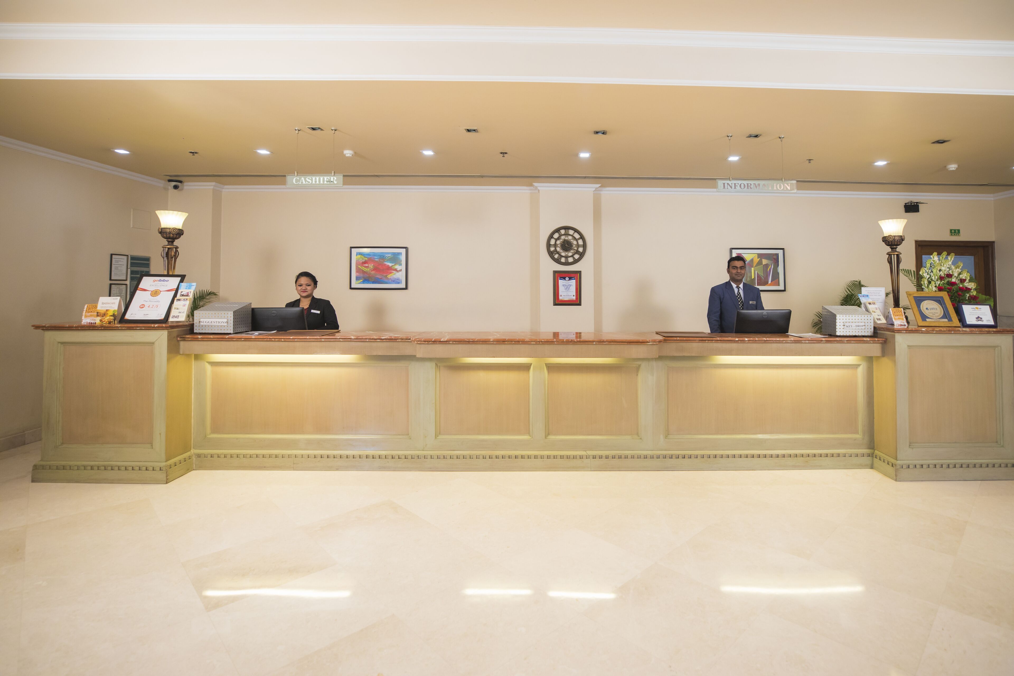 A reception desk with two staff members, a framed certificate, and a sign indicating 'Cashier' and 'Information' areas.