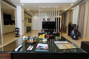 Una sala de estar moderna con una mesa de centro de vidrio, un televisor de pantalla plana y un comedor con un frutero.