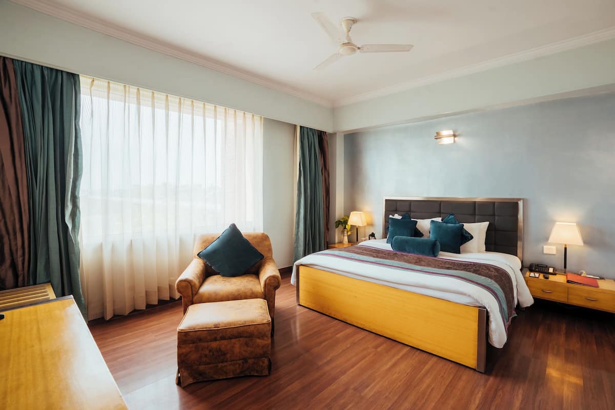 Quarto de hotel com cama, cadeira, escrivaninha e mesa de cabeceira.