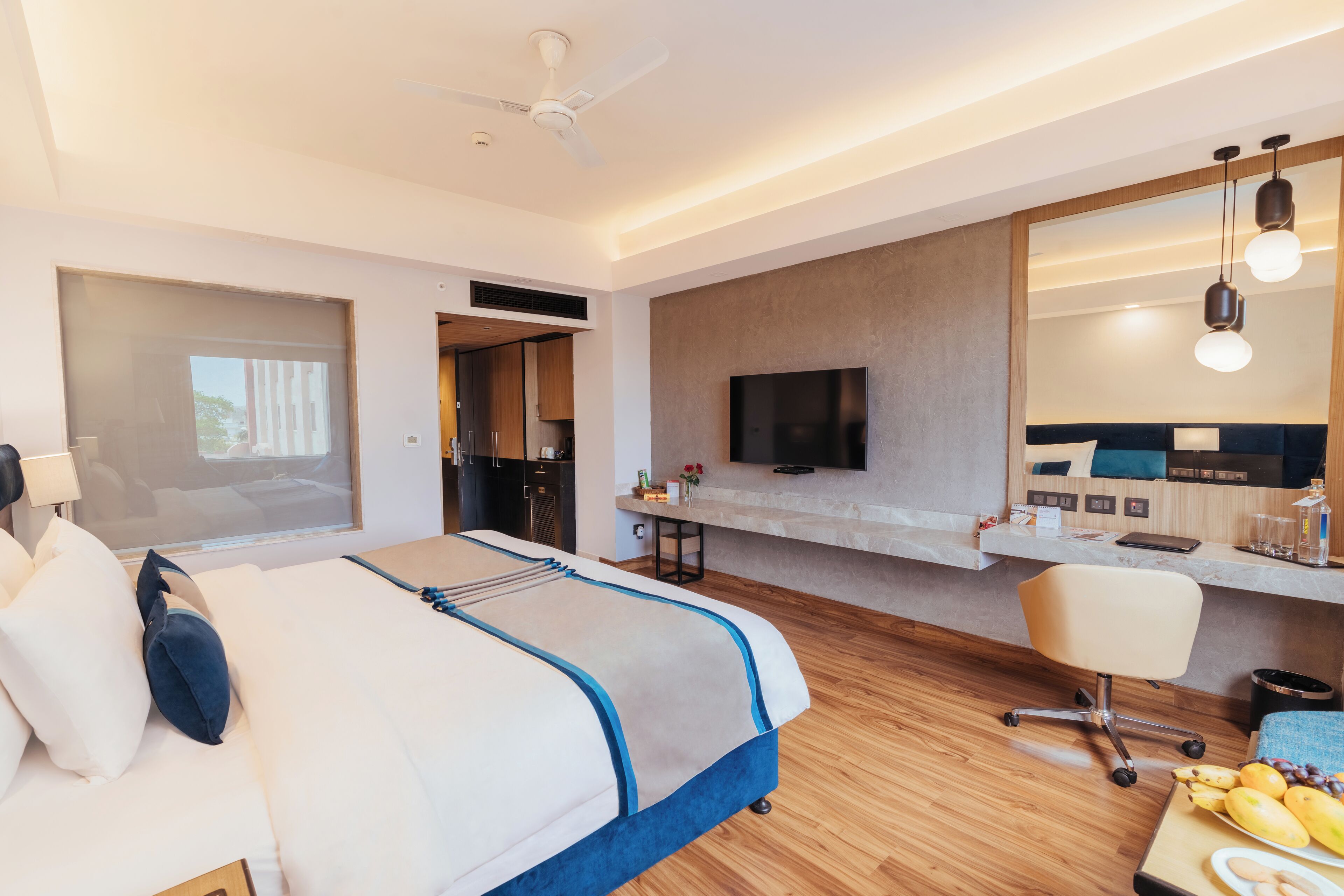A modern hotel room with a large bed, a desk, a television, and a mirror.