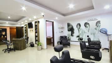 A salon with a reception desk, several hairdressing chairs, a L'Oréal Professional poster, and a potted plant.
