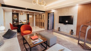 A modern living room with a sofa, coffee table, and orange chairs. There is a dining area with a table and chairs, and a TV mounted on the wall. - The Piccadily Lucknow (Lucknow)