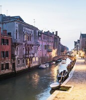 Un canale con edifici storici, un ponte e imbarcazioni ormeggiate lungo l'acqua.