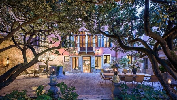 A courtyard with a dining area, a building with large windows, and a tree in the foreground. - Hotel Heureka  (Venice)