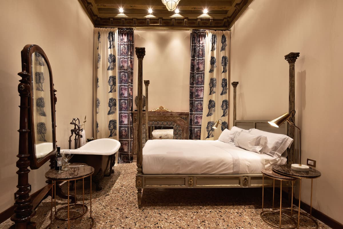 A bedroom with a bed, a vanity with a mirror, a bathtub, and a chandelier.