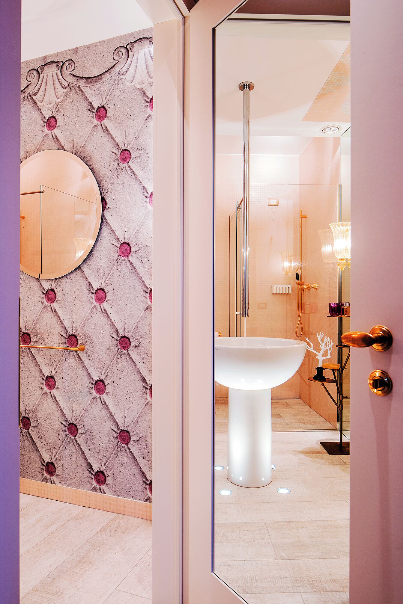 Un baño con un espejo redondo, un lavamanos pedestal y una cabina de ducha de vidrio.