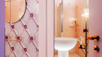 Un baño con un espejo redondo, un lavamanos pedestal y una cabina de ducha de vidrio.