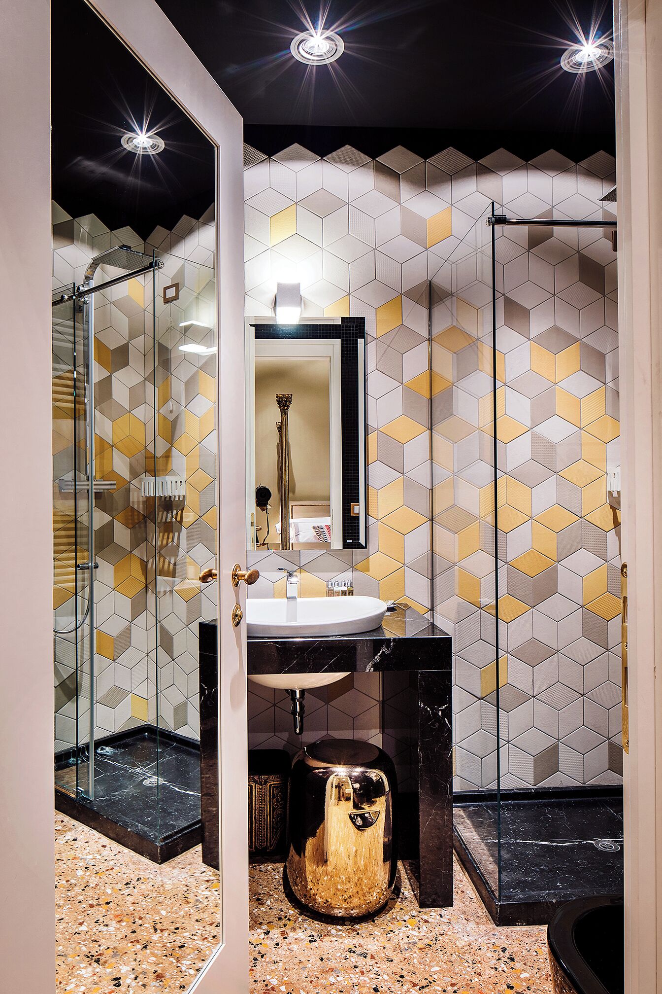 Un baño moderno con cabina de ducha de vidrio, un lavabo con encimera de mármol y un revestimiento de pared con estampado geométrico.