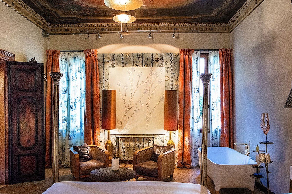 A room with a fireplace, two armchairs, a bed, and a bathtub.