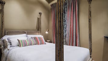 A neatly made bed with a headboard, a bedside lamp, and patterned curtains.