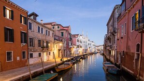 A narrow canal flanked by historic buildings with boats docked along the water. - Hotel Heureka  (Venice)