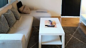 Moderni olohuone, jossa on beigenvärinen sohva, valkoinen sohvapöytä ja taulu seinällä.