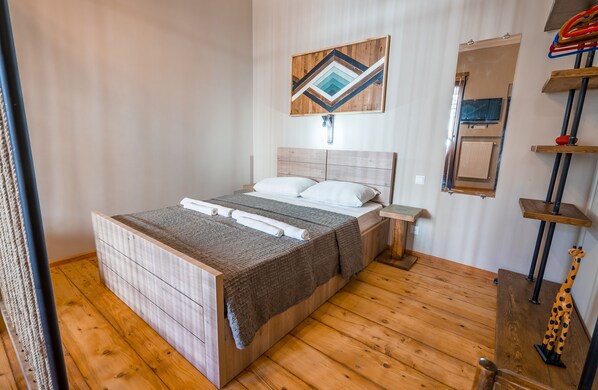 Ein Schlafzimmer mit einem Holzbett, einem Nachttisch, einem an der Wand befestigten Fernseher und einem Regal mit Dekoration.