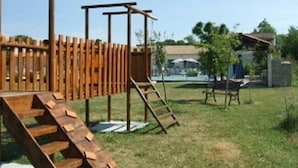 Una estructura de juego de madera con una escalera y un tobogán en un jardín trasero cubierto de césped.