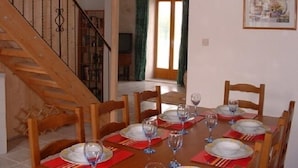 Un comedor con una mesa de madera dispuesta para seis personas, rodeada de sillas de madera. A la izquierda, se ve una escalera con barandilla de metal.