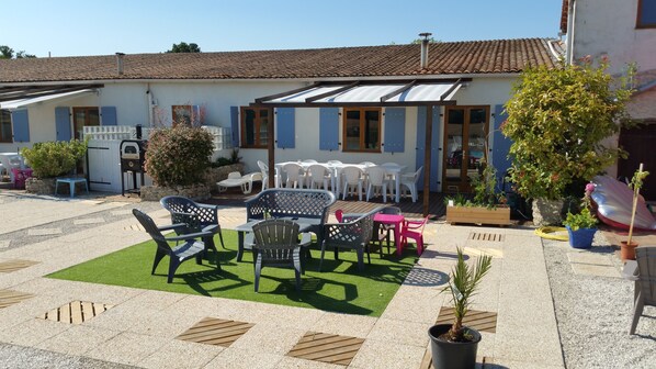 A patio area with outdoor seating, a small garden, and a building with a tiled roof. - Gite La Grange - Logis de la Croix (Gibourne)