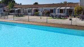 A swimming pool with a wooden deck and a fenced patio area with outdoor seating. - Gite La Grange - Logis de la Croix (Gibourne)
