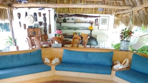 A room with a curved sofa set, a decorative rug with a seahorse design, and a thatched roof. - Casa Don Pepe (Barra de Potosi)